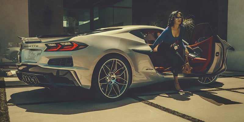 Woman in dark blue top and pants exiting or entering a silver Corvette C8 with a red interior.