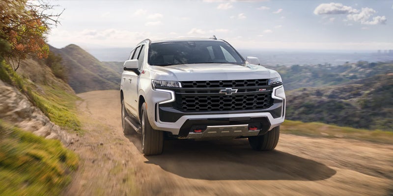 White Chevrolet Tahoe Z71 SUV driving on a dirt road through hills, with a city visible in the distant valley.
