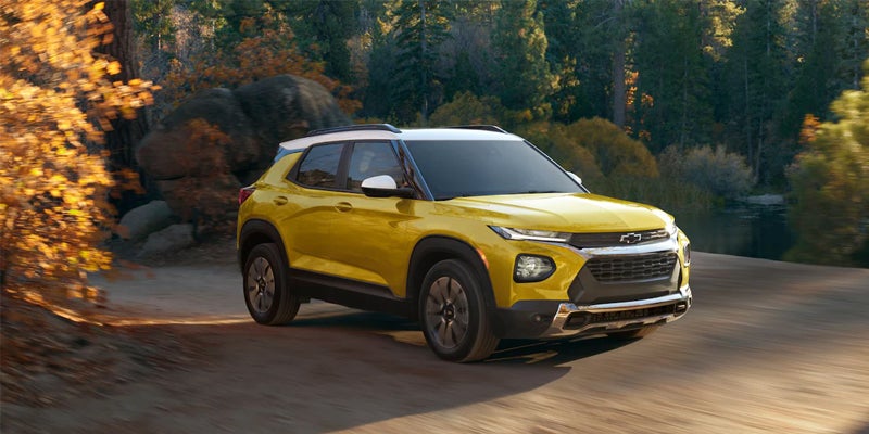 Yellow Chevrolet Trailblazer with a white roof driving on a dirt road through a forest with autumn foliage.