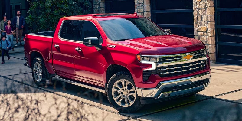 Red Chevy Silverado pickup truck parked on a driveway with a family walking towards it in the background.