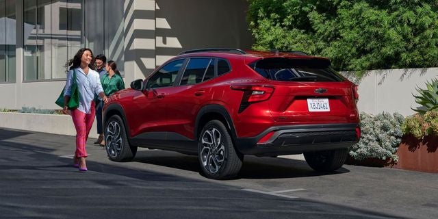 Red Chevy Trax SUV parked with a smiling woman walking towards it and two people by the rear passenger door.