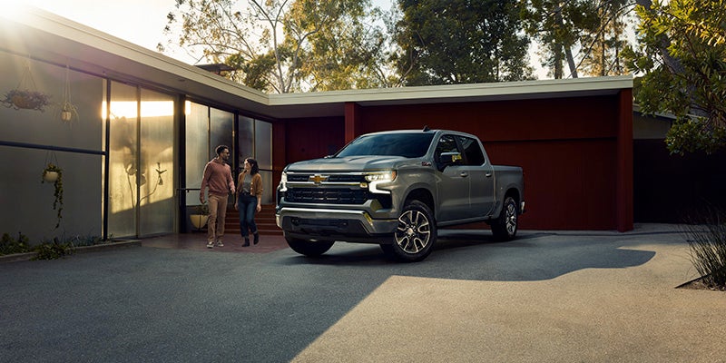 Gray Chevrolet Silverado truck parked in a modern driveway as a couple walks out of the house.