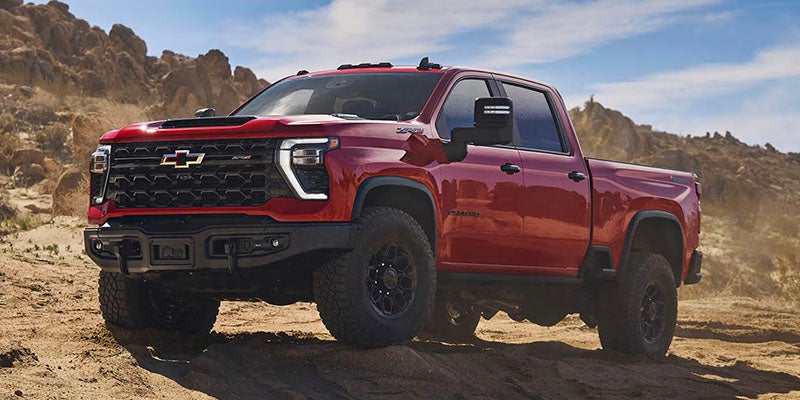 Red Chevrolet pickup truck with large tires on a dirt trail in a rocky, desert landscape.