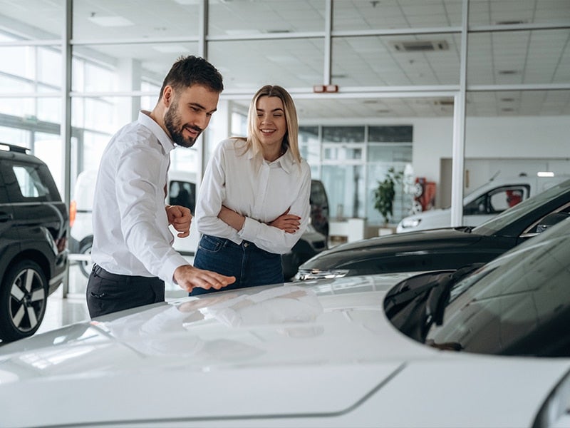 Smiling couple in a car dealership, with the man pointing at the hood of a white car.