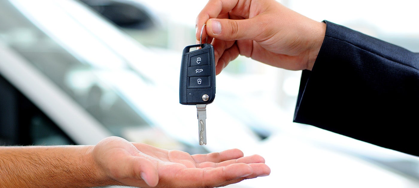 A hand in a dark suit jacket hands a modern car key to another person's open palm.
