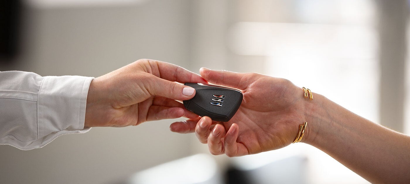 A hand holding car keys above an open receiving hand, against a pink background.