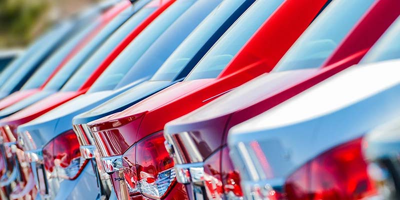 Row of new cars, alternating red and white, seen from the rear and side in a dealership lot.